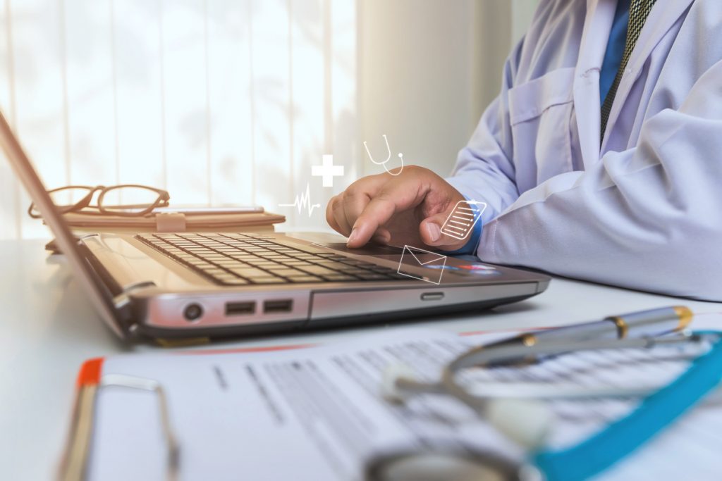 doctor using laptop with medical icons floating above keyboard